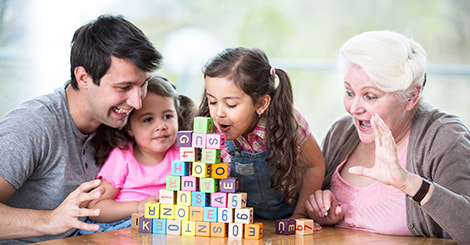 Father and two daughters playing alphabet blocks together with their grandmother photo